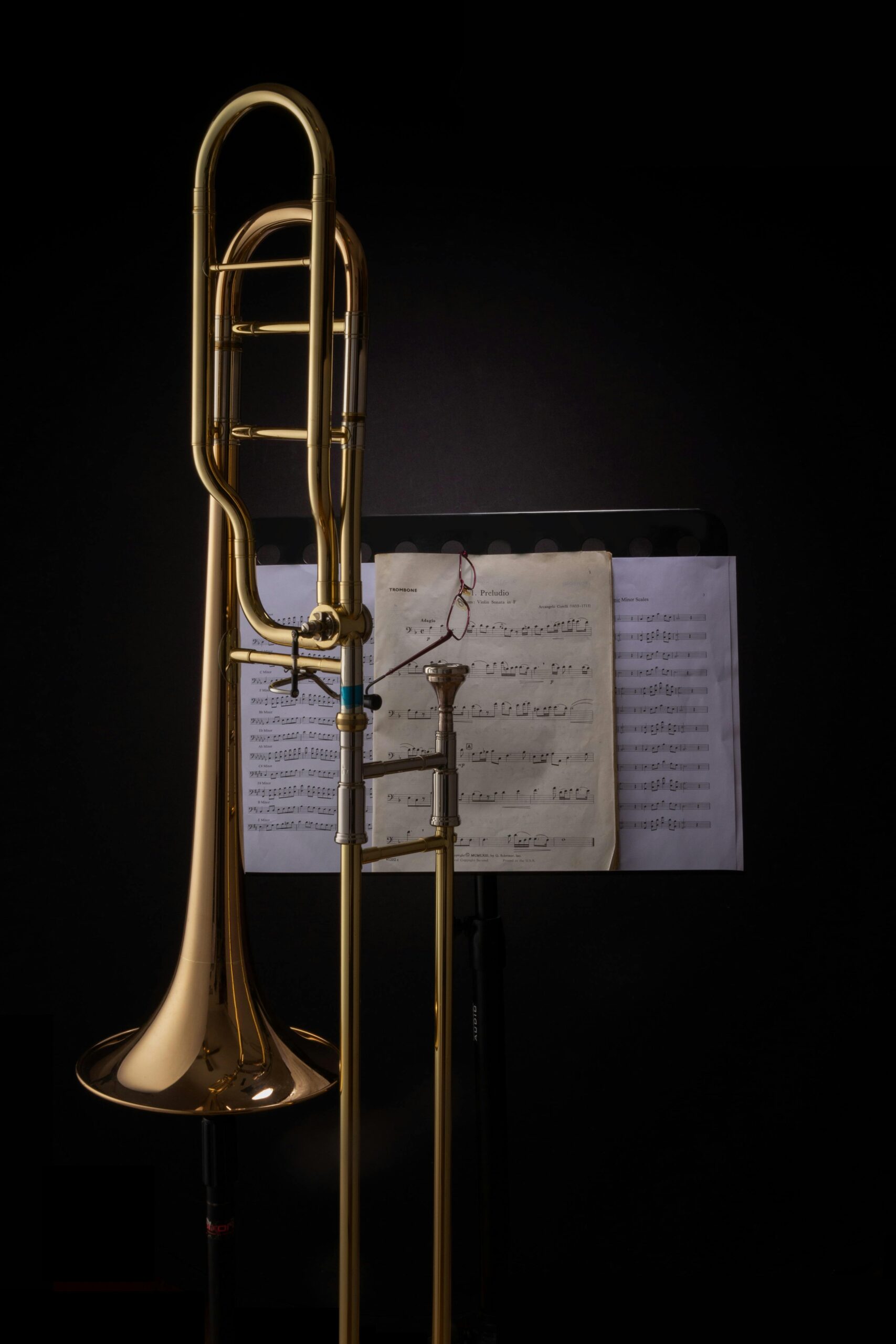 A trombone standing beside sheet music in a dark studio, showcasing musical artistry.